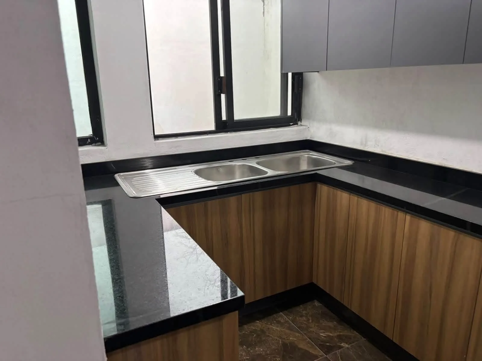 Cocina con cubierta negra, tarja doble y mobiliario de madera